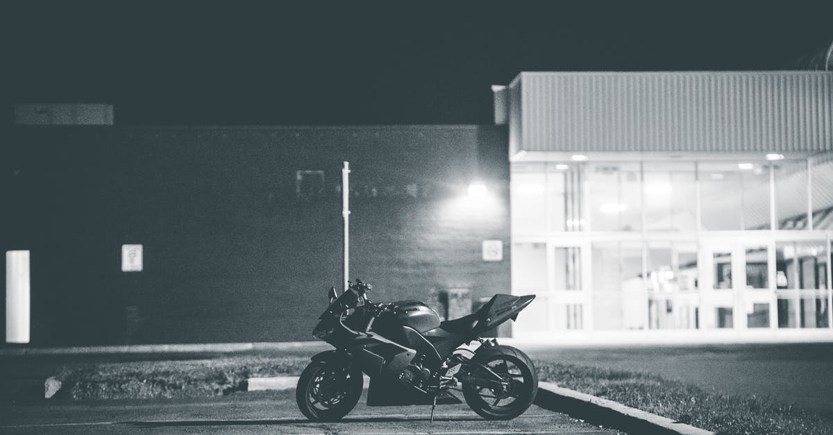 Canada: Entry by vehicle - Black and white of stylish motorcycle parked on asphalt surface on local street of city at night