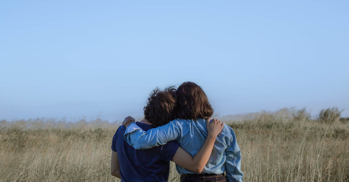 Canada visitor visa proof of relationship with inviting friend - Back view unrecognizable girlfriends wearing casual clothes hugging each other while standing on grassy vast field in summer countryside