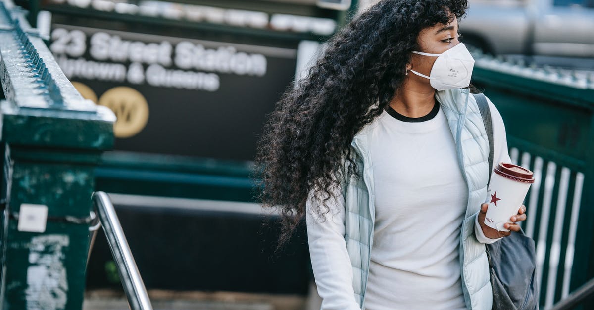 Canadian citizen staying in the US - Emotionless African American female with coffee to go wearing casual wear and protective face mask leaving underground station and looking away in New York City