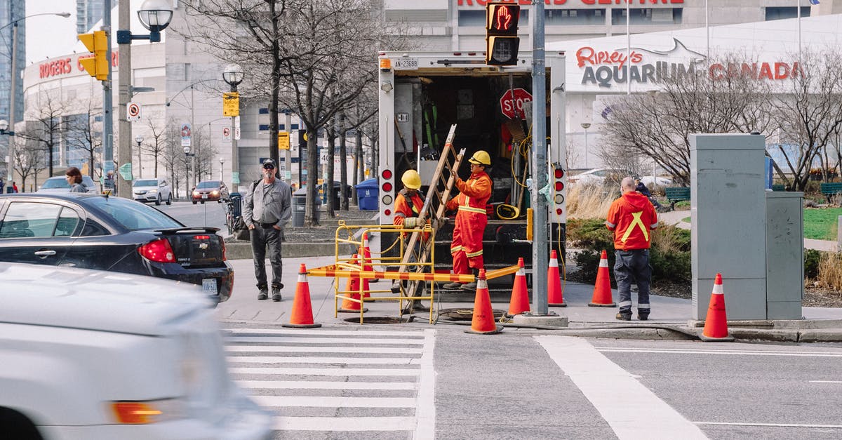 Canadian renting car in Finland and driving sports team members - Full body of workers in red uniforms and yellow helmets carrying wooden ladder in street near automobile road