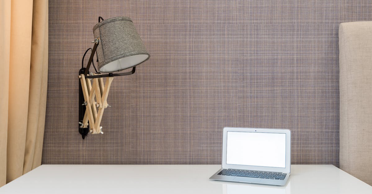 Cancel a Hotel Room After Checking in Online - Interior of workplace with opened netbook on white table near wall with lamp