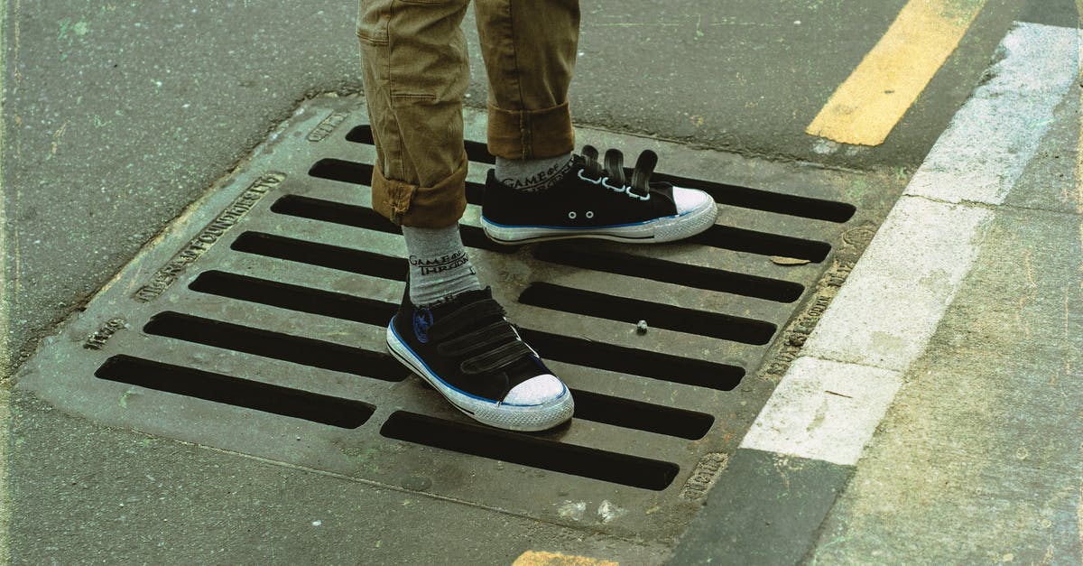 Cancellation of last leg of flight, can I still fly? - From above crop anonymous male legs in casual wear standing on asphalt road sewerage steel grating in daylight