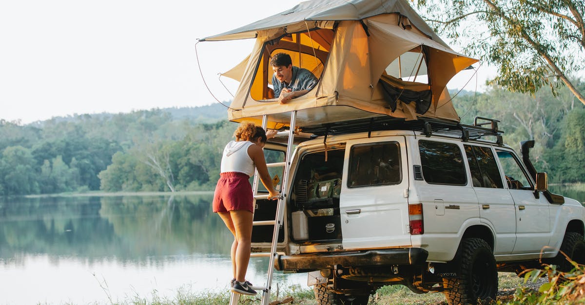 Car mask rules in Italy when living together during holiday - Unrecognizable woman standing on ladder near boyfriend recreating in tent during camping at lakeside