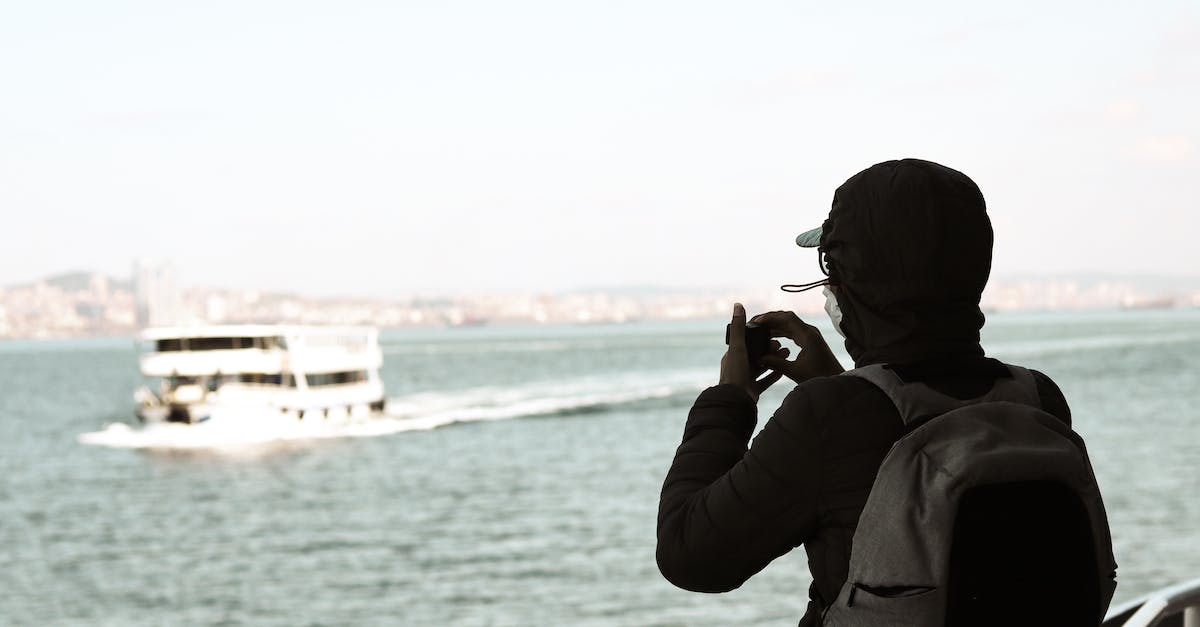 Caribbean cruise for the backpacker? - Back view of unrecognizable man with backpack in jacket admiring ship in wavy sea using small camera