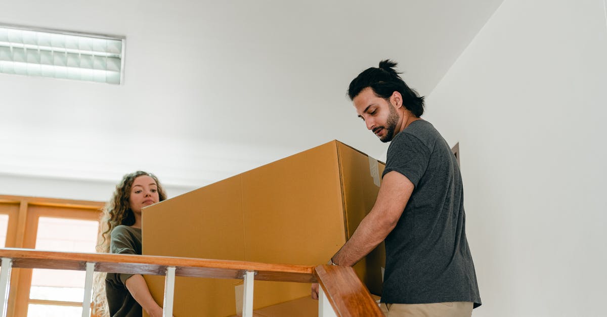 Carry bicycle into the US as personal item - From below of couple in casual clothes carrying big carton box together while moving packed personal items into new apartment