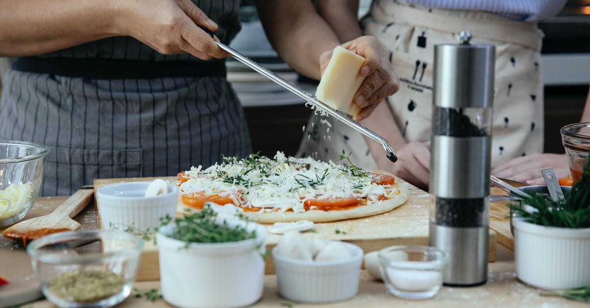 Carry on cheese grater on domestic U.S. flight? - Unrecognizable female cooks grating cheese on homemade pizza at table with various ingredients and condiments in kitchen during cooking process