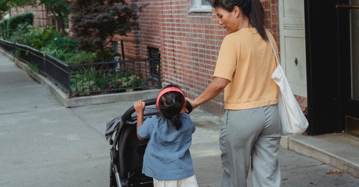 Carry Stroller on Emirates flight without a kid? - Back view of ethnic woman carrying stroller with little girl on sidewalk of street