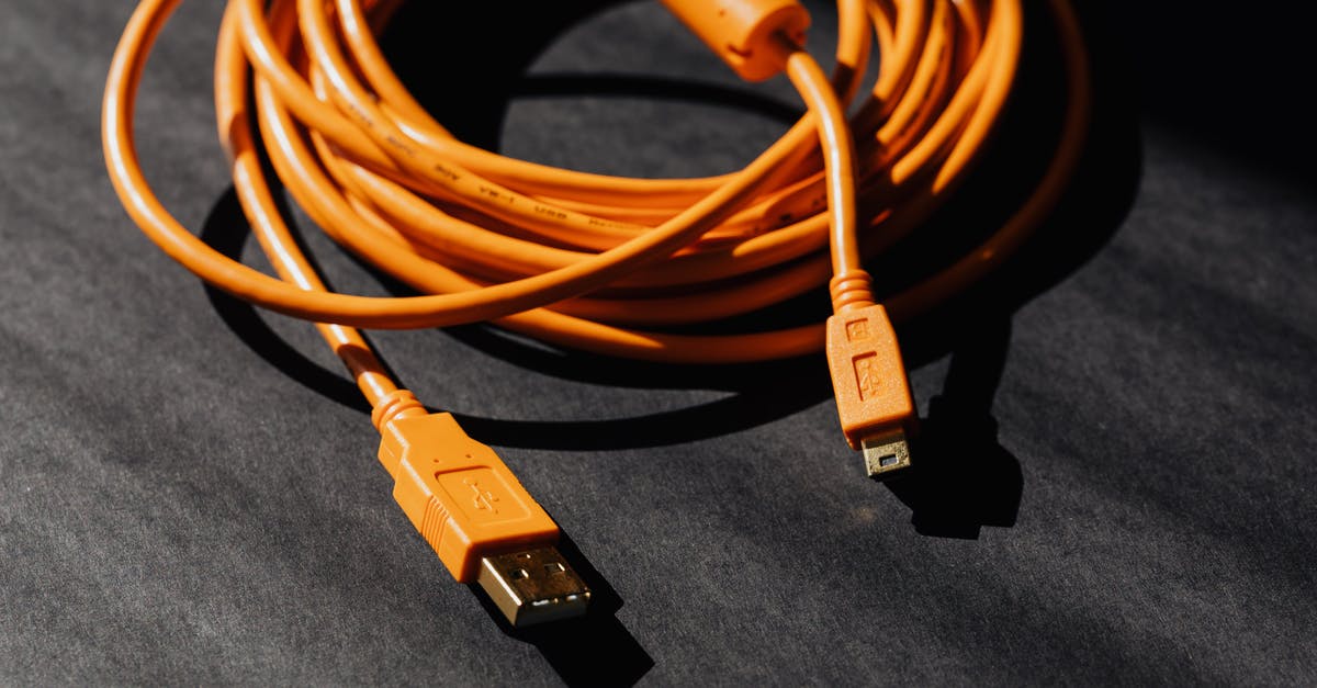 Carrying a laptop battery with a cracked case onto a flight - From above of orange usb to micro usb cable twisted into ring placed on black board