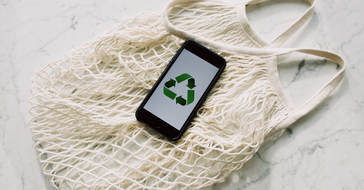 Carrying a UPS Return Package with Phones, from the US and back - Overhead of smartphone with simple recycling sign on screen placed on white eco friendly mesh bag on marble table in room