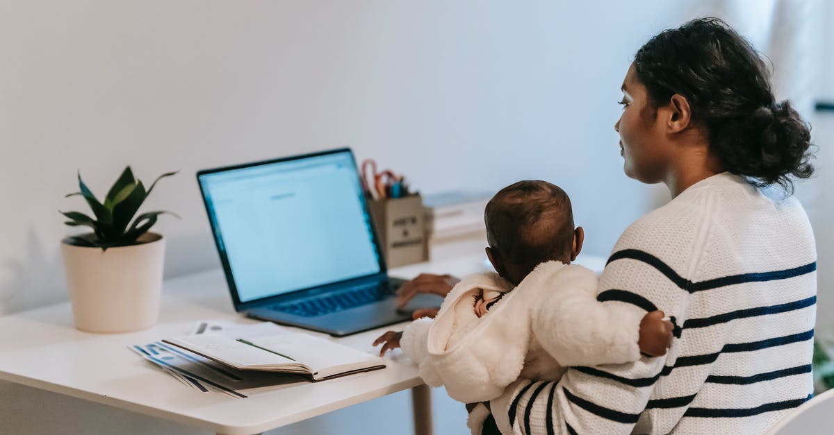 Carrying my laptop to abroad from India - Pensive ethnic woman in casual clothes slitting with baby while browsing netbook in light room in apartment in daytime