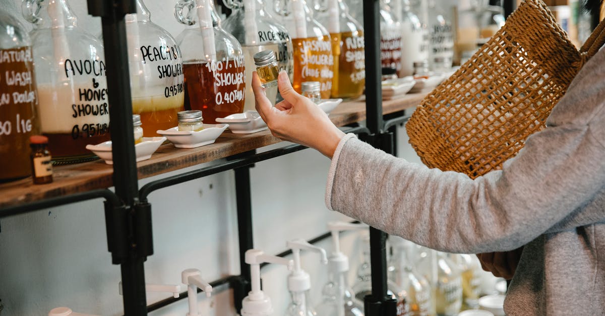 Carry-on liquids in toiletry bag (not clear ziplock)? - Crop customer examining glass jar with shampoo in market while standing near big dispensers placed on wooden shelves