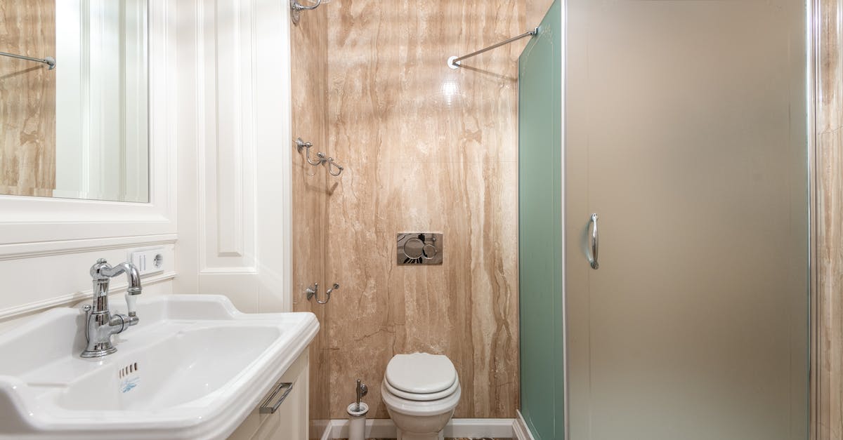 Cast iron pot in cabin luggage? - Interior of bathroom with wall mounted toilet and shower cabin at tiled wall near clean sink under bright lighting