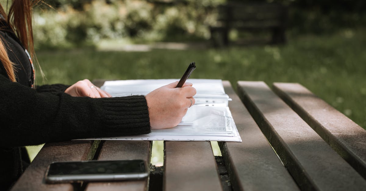 Cell phone data plan recomendations? - Anonymous female in casual clothing writing in copybook on wooden bench in sunlight on blurred background