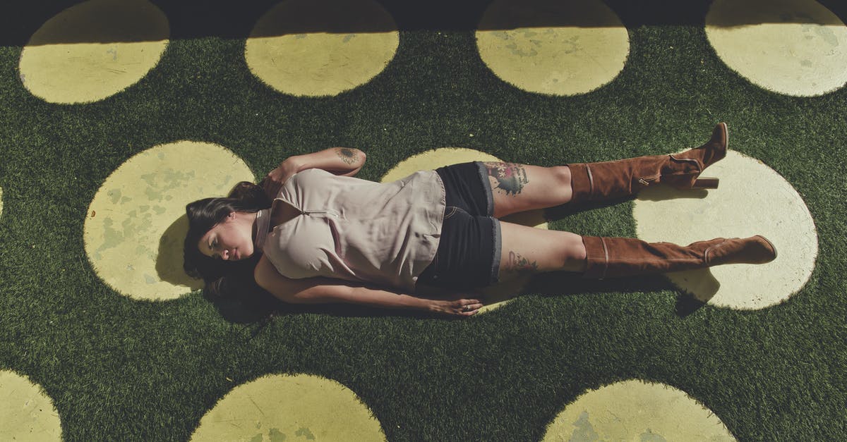 Chaining same day round trips - High angle full body of young woman in casual clothes and brown boots lying alone on green grass with yellow circles in sunny summer day and looking away