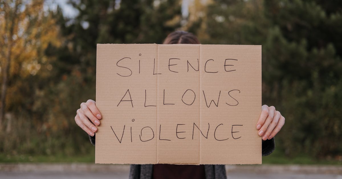 Change of Occupation Notice - Anonymous person showing slogan silence allows violence on cardboard on road near green trees