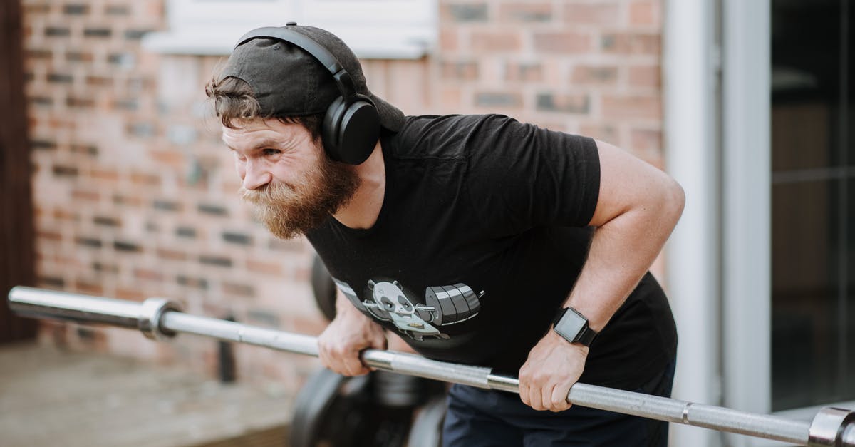 Change trains in Brest (Belarus) under 15 minutes? - Brutal male with headphones pulling massive metal barbell on blurred background of brick house