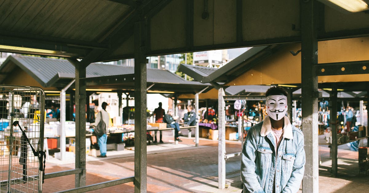 Changes to British transit visa policy - Unrecognizable black man in stylish clothes and Anonymous mask standing in local market in city and looking at camera in sunny day