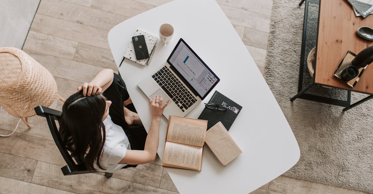 Changing UK visa from visitor to study - From above of young woman with long dark hair in casual clothes working at table and browsing netbook while sitting in modern workplace and touching hair