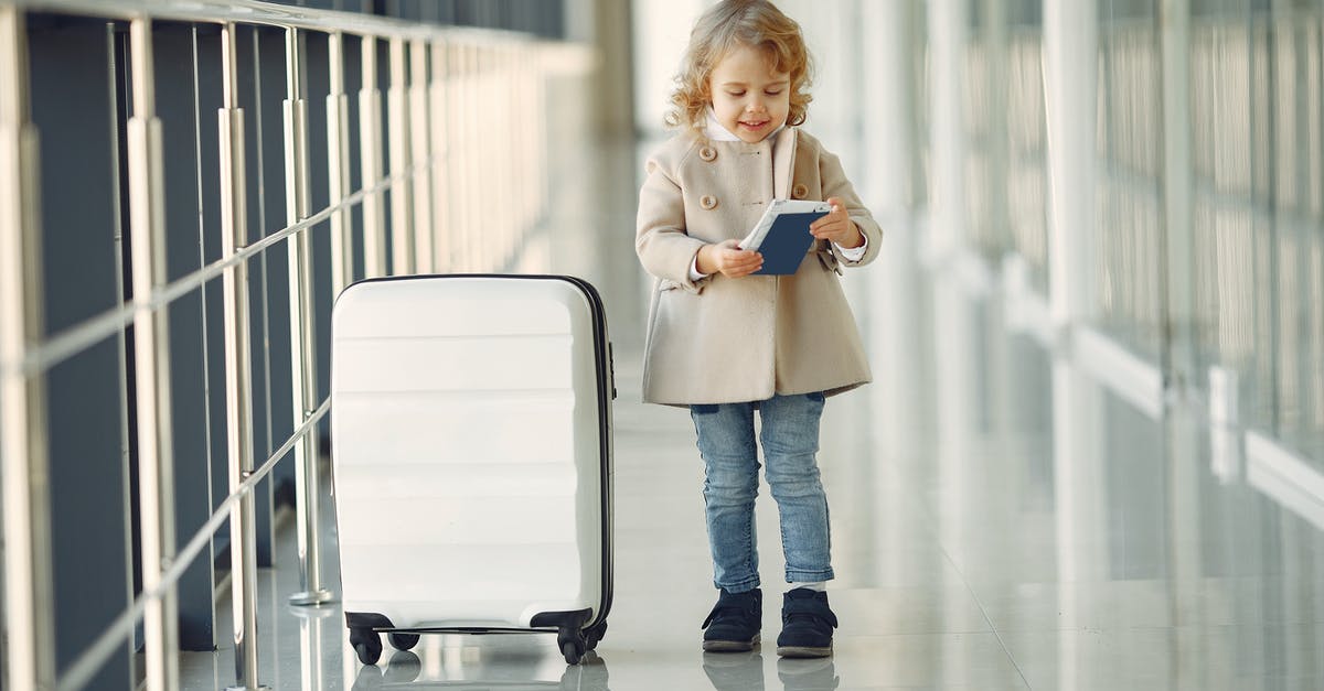 Charged checked baggages for connecting international flights - Full body of smiling cute little girl in jeans and beige coat standing near suitcase and checking information in documents