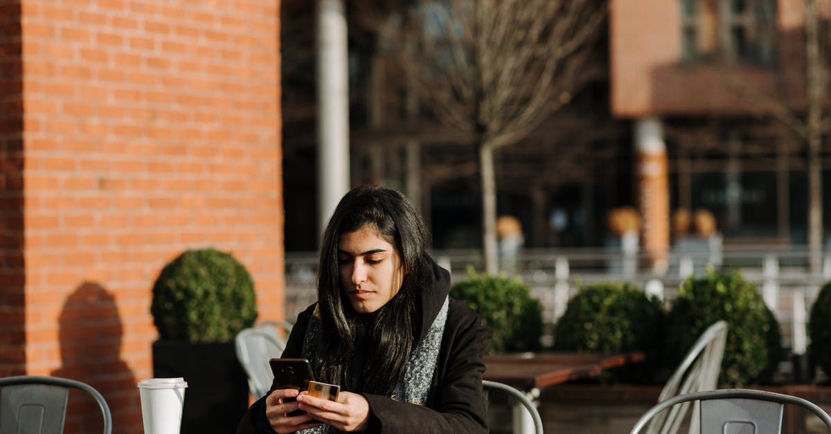 Charges when using a Euro country debit card in Budapest - Young attentive Hispanic female buyer with cellphone and credit card shopping online in urban cafeteria