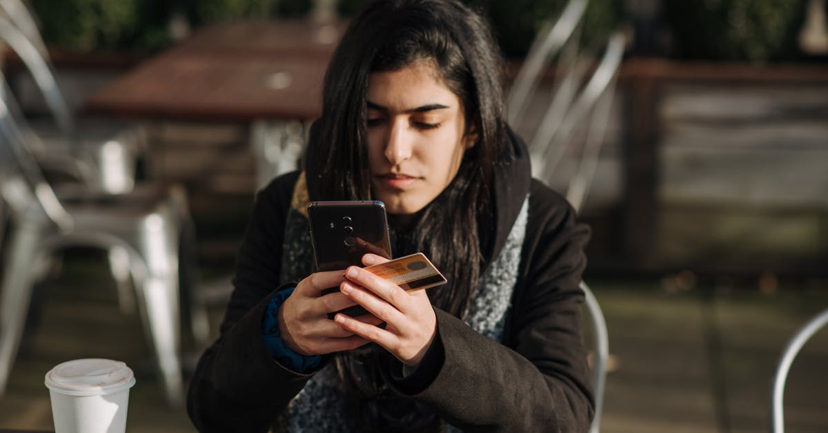 Charges when using a Euro country debit card in Budapest - Young ethnic female purchaser with credit card shopping online on mobile phone at table with takeaway hot drink in cafeteria