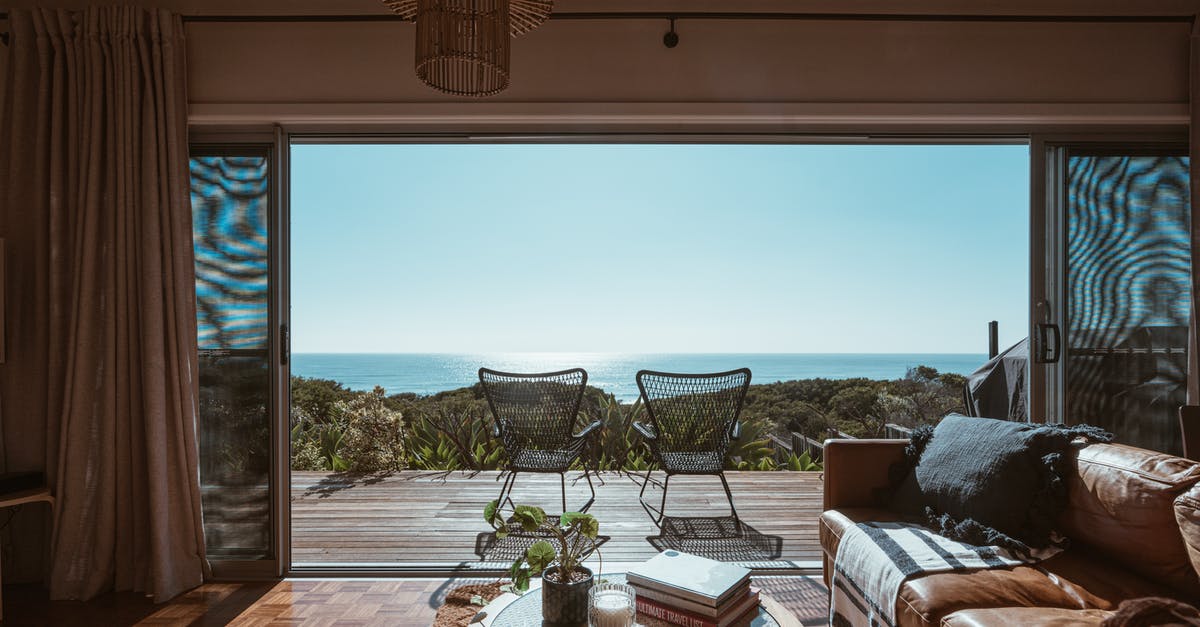 Cheap accommodation in Spain - Interior design of luxurious apartment with large balcony doors and wooden terrace having picturesque view on green forested seashore and calm blue sea