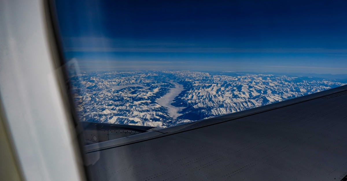 cheap air travel tickets through blind company - Through window wing of modern airplane flying in blue sky over river flowing through mountainous terrain on sunny day