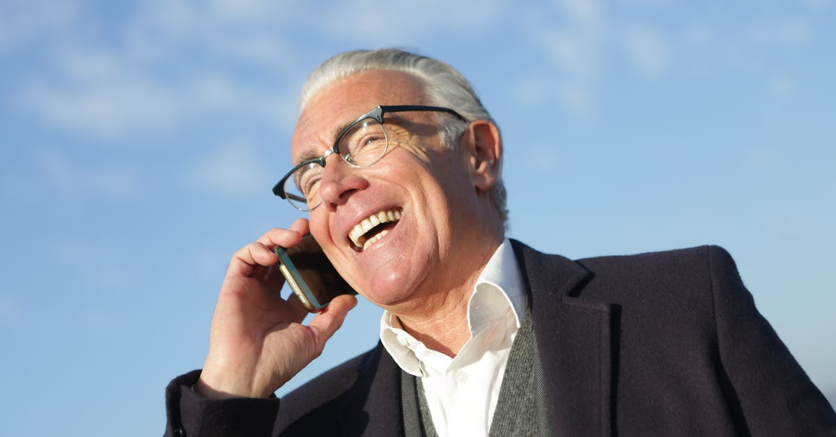 Cheap phone calls from Canada to Poland - From below of delighted aged male entrepreneur in classy outfit standing on street and speaking on cellphone while laughing and looking away