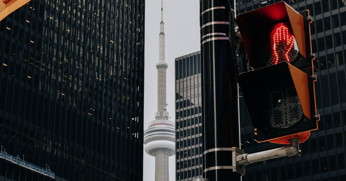 Cheap travel to Toronto from California - Traffic light with red color and TV tower between skyscrapers