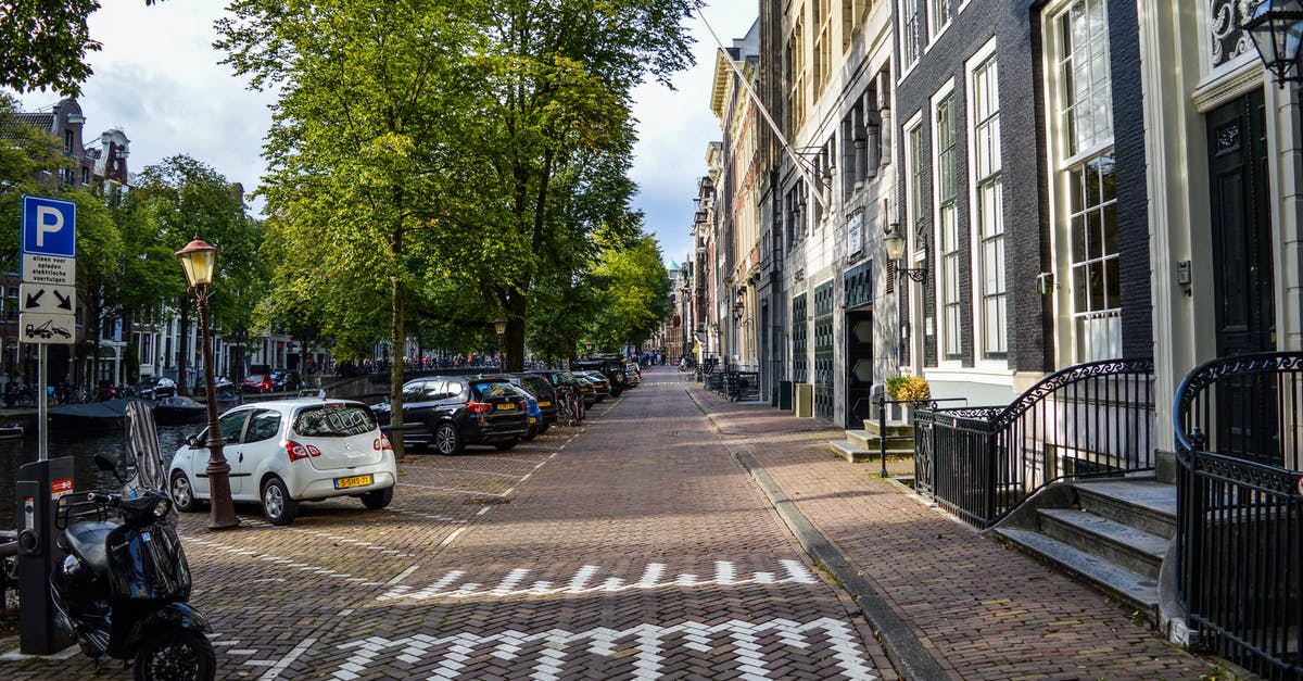 Cheap way to get from Amsterdam to Prague: train? - Empty paved bicycle road and sidewalk between aged residential buildings and canal in sunny morning in Amsterdam