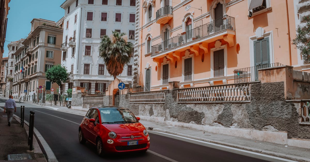 Cheapest hotel in Europe - Red 5-door Hatchback On A Narrow Street Lined With Apartment Buildings