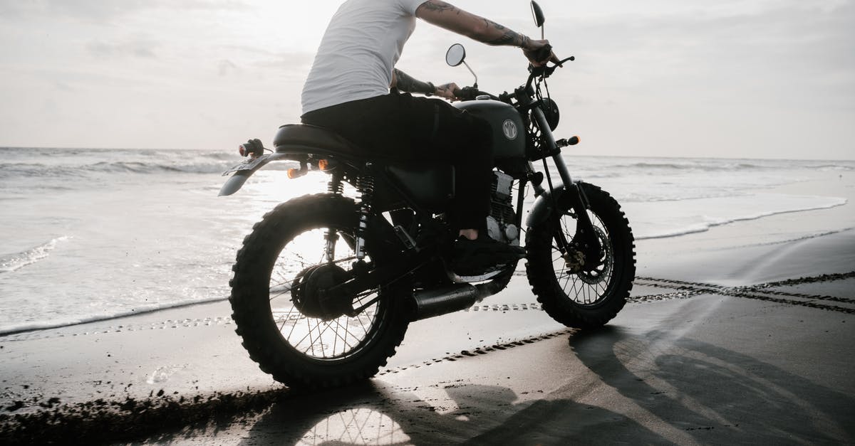 Cheapest ride from Raja Ferry to Chaweng Beach [closed] - From below side view of unrecognizable tattooed guy in t shirt riding motorbike on sand beach leaving traces and creating splash effect near sea in evening in back lit