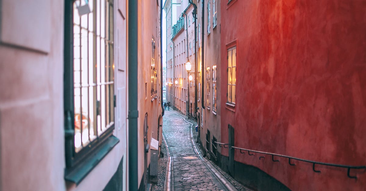 Cheapest Way to Get to Europe--I'm Flexible [duplicate] - Narrow cobblestone pedestrian passage between old apartment buildings with burning electric lights in windows at twilight