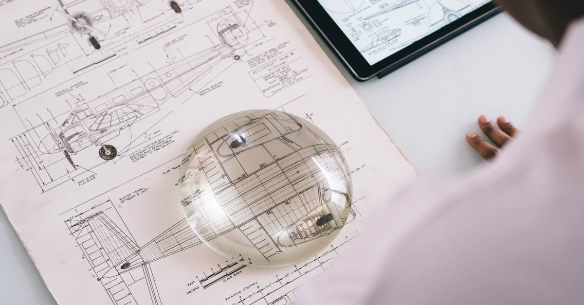 Check in to conflicting flights - Crop unrecognizable mechanic holding magnifying glass on paper with airplane drawing while working on project on tablet in aircraft factory