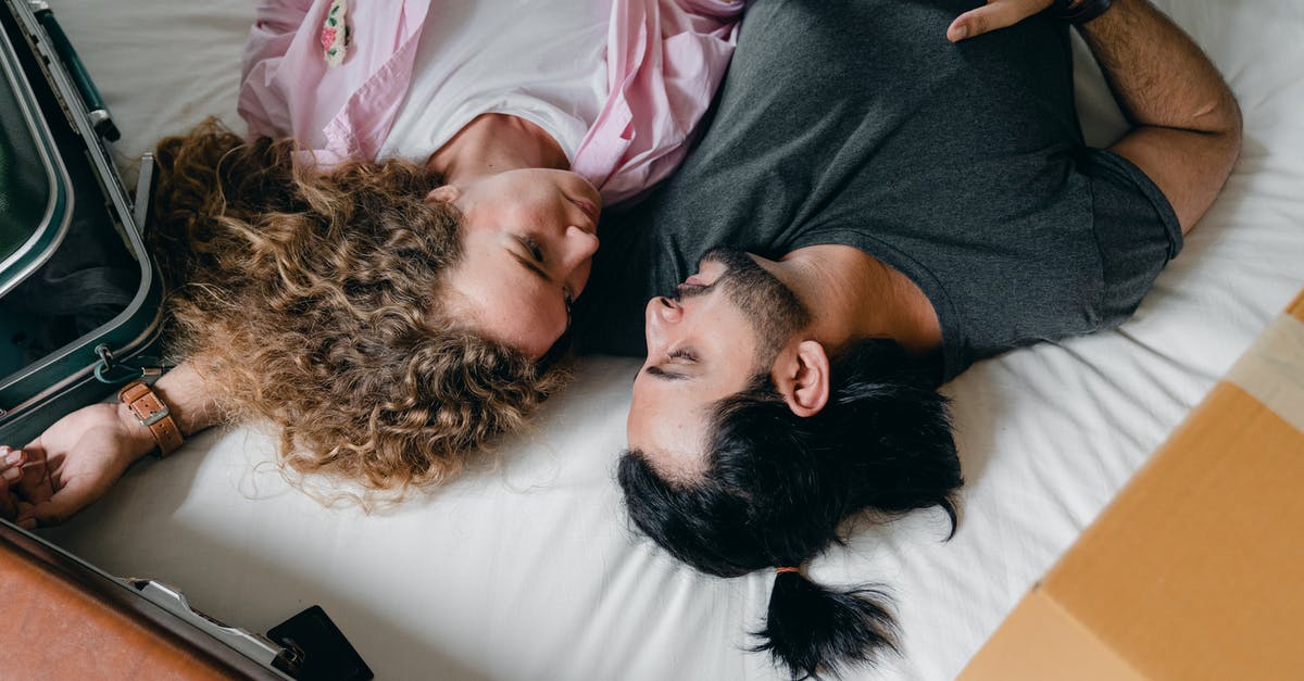 Checked baggage on a Domestic → Domestic (connection) → International transit? - From above of multiethnic couple in casual clothes lying near suitcases on bed while resting and hugging during moving into new apartment