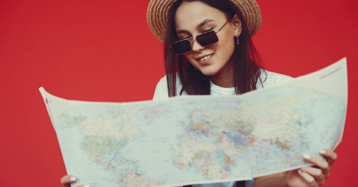 Checked baggage size limits - Smiling young woman in stylish hat and sunglasses choosing destination on paper map while standing with luggage on red background