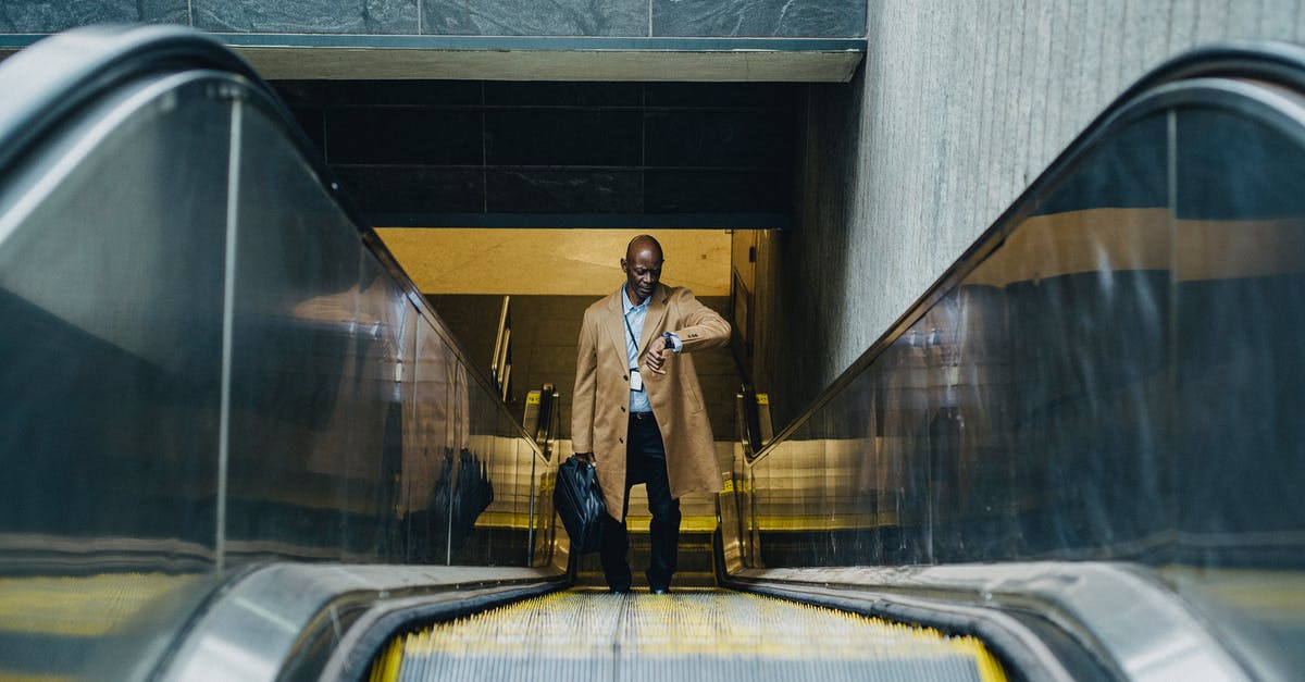 Checked baggage through TSA carry-on security when late for check-in? - Contemplative black businessman riding escalator and looking at wristwatch