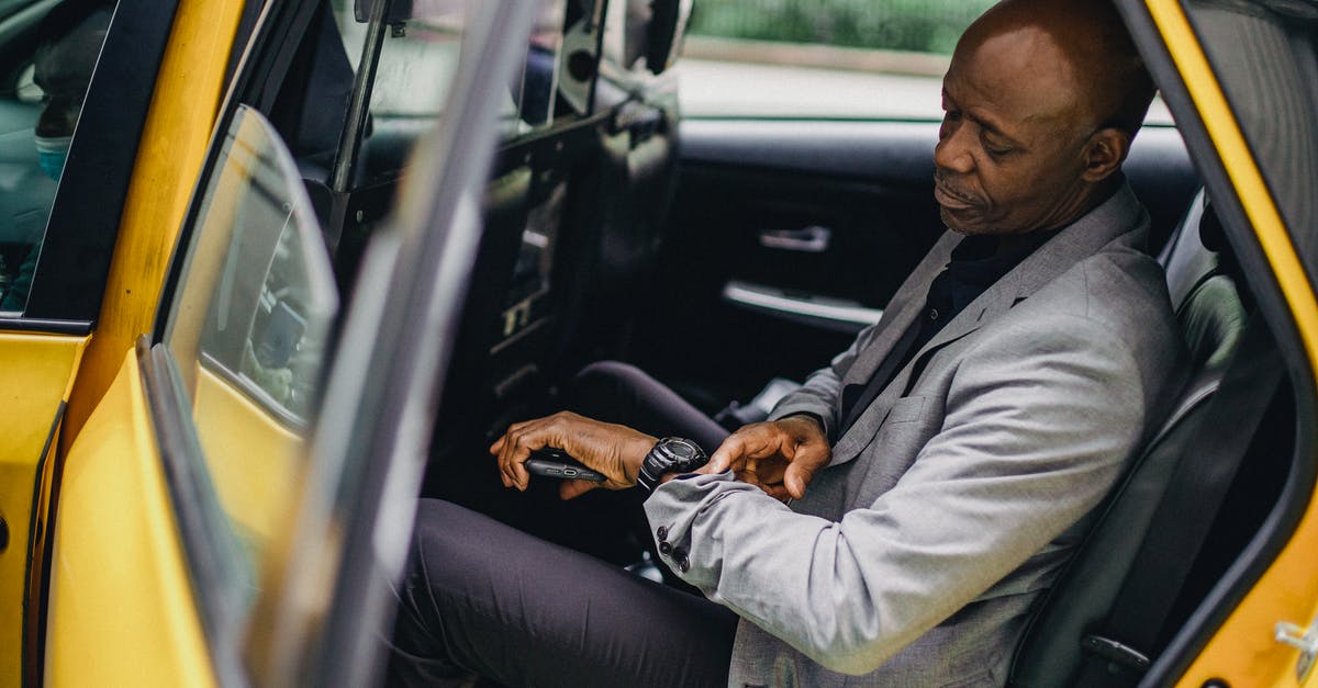 Checked baggage through TSA carry-on security when late for check-in? - Serious black businessman checking time on wristwatch in taxi