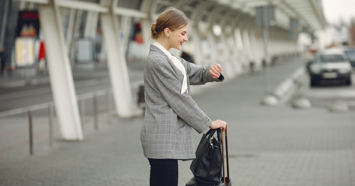 Checked in Baggage transfer Dubai T2 to T3 [closed] - Cheerful female manager checking time on wristwatch standing with bags near bus station