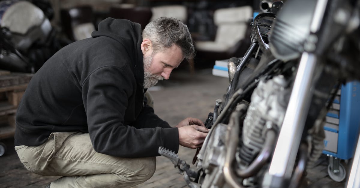 Checking a hire bike is properly docked - Side view of focused male mechanic in casual wear sitting near motorbike and examining details details in workshop