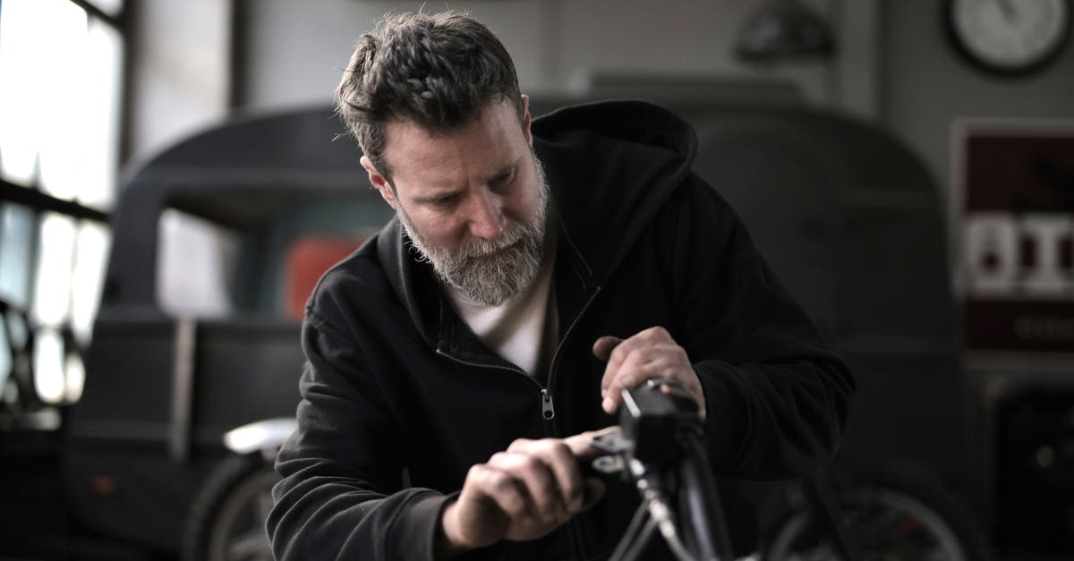 Checking a hire bike is properly docked - Concentrated male biker in casual wear fixing motorcycle part while working in garage