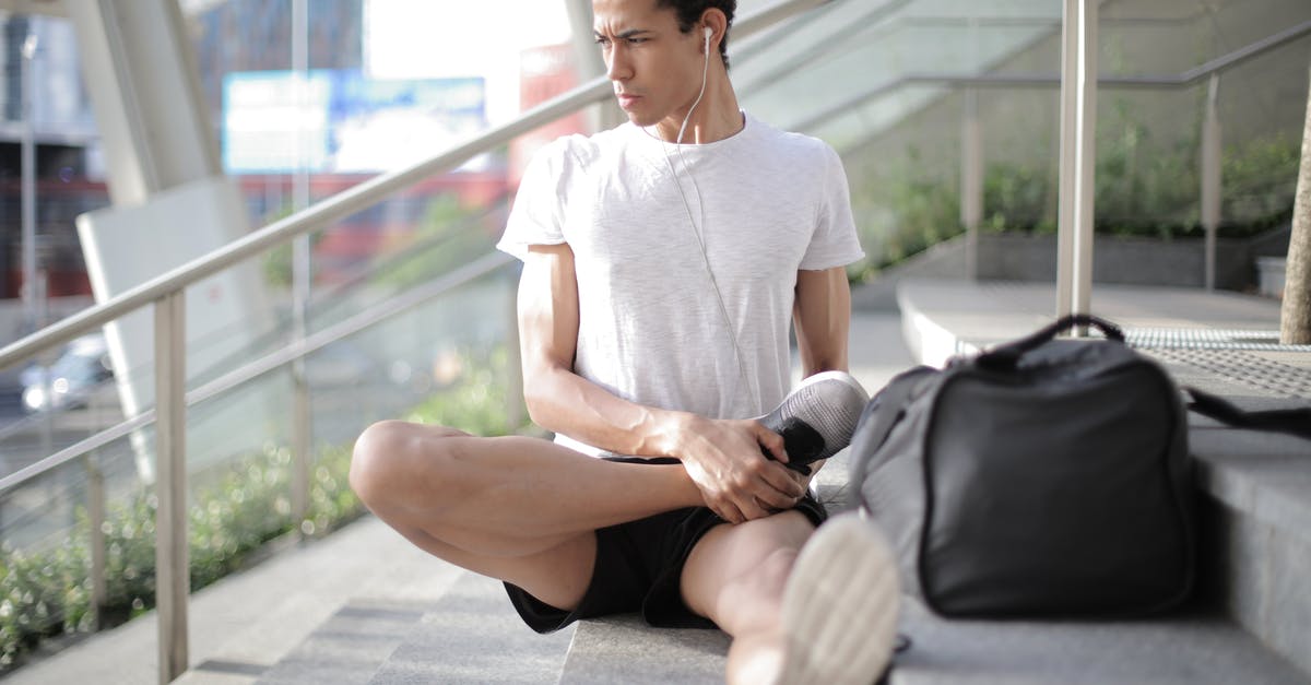 Checking In Luggage During Intermediate Leg [duplicate] - Young ethnic athlete in earbuds stretching body while sitting on stairs at entrance of contemporary building