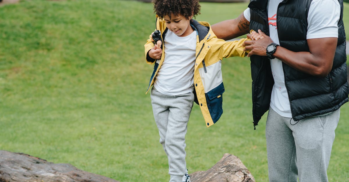 Checking MetroCard balance outside? - Caring African American man holding hands of careful kid while walking on wooden log in grassy park on blurred background