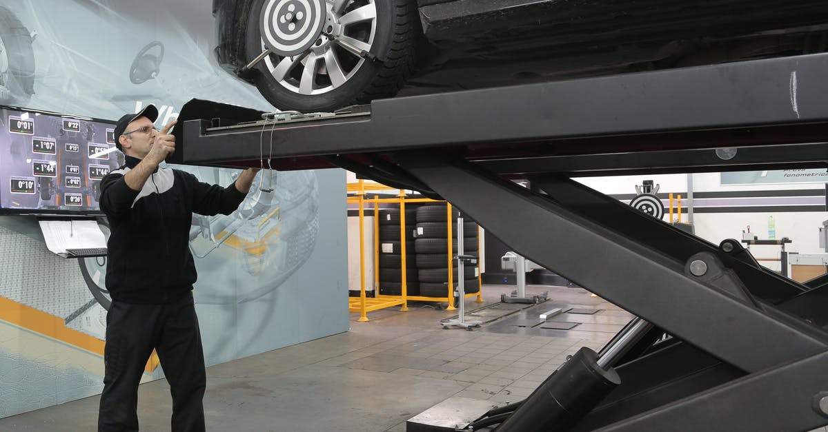 Checking ski equipment on plane - Serious mechanic checking car wheels on lift in modern car service garage