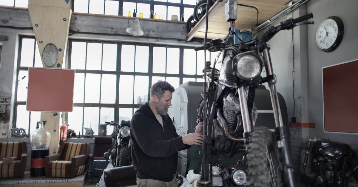 Checking ski equipment on plane - Side view of bearded adult mechanic in casual uniform standing near motorcycle and working with engine in workshop