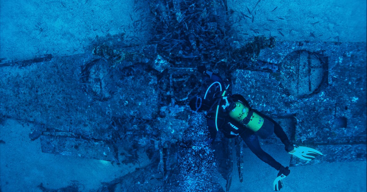 Checking ski equipment on plane - Top view of unrecognizable person in wetsuit inspecting rough remains of sunken plane on bottom of sea