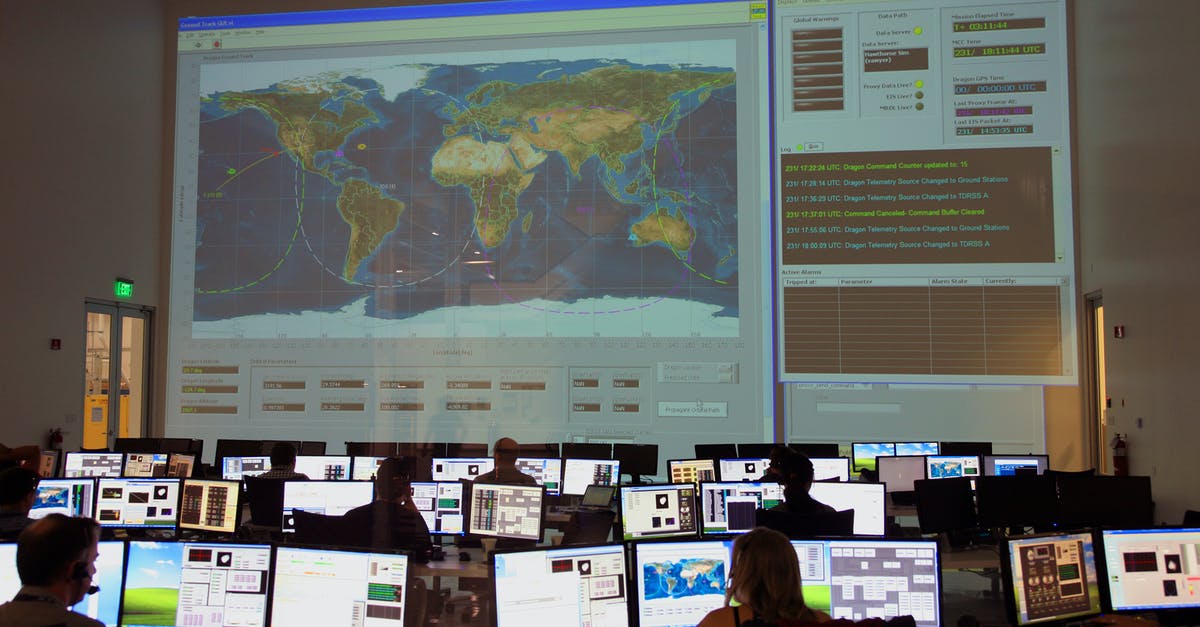 Checking-in for an intercontinental flight with intra-continental connection - Back view of unrecognizable employees working on computers in flight control room with big interactive map on wall and analyzing data