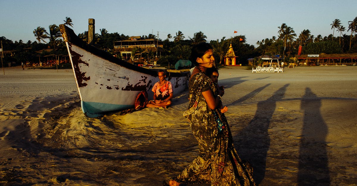 Child travel consent form for domestic travel within India - Indian woman carrying baby along sandy beach near shabby boat