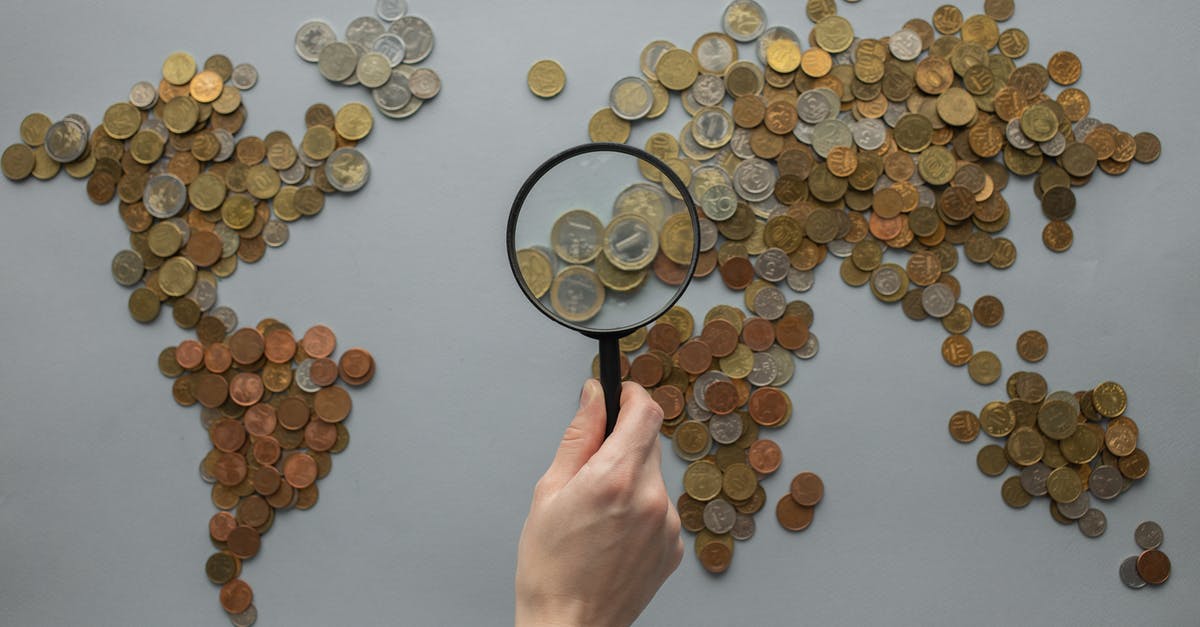 Child travelling abroad and money - Anonymous person with magnifying glass over world map of coins