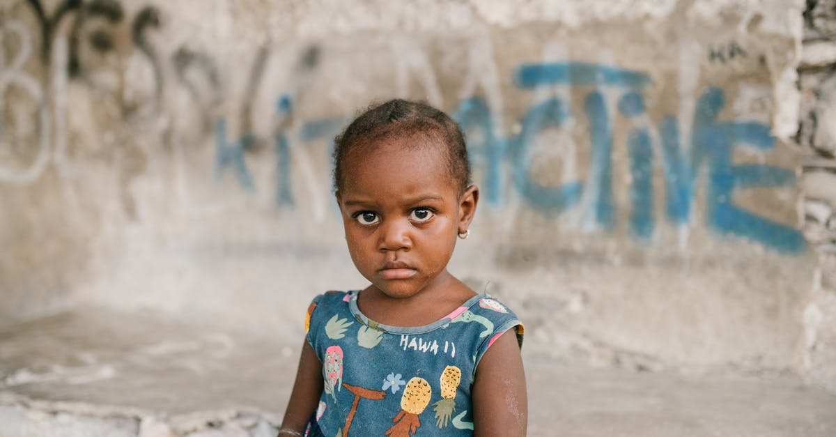 Children free under 5 on UK trains -- any need to prove? - Frowning African American girl near weathered concrete building with vandal graffiti and broken wall in poor district